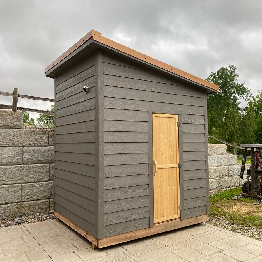 Exterior of a sauna cabin with a copper roof edge on a stone patio